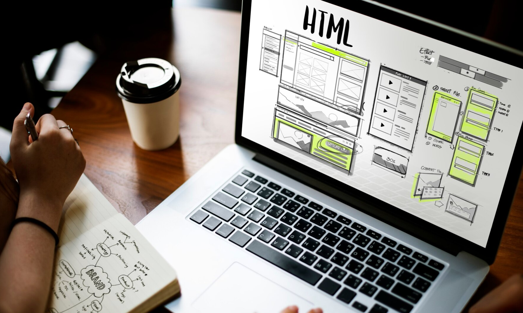 Workspace with laptop showing a wireframe on screen, coffee cup, and notebook with brand strategy notes.
